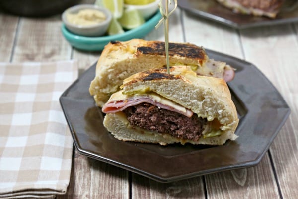 This Cuban Style Burger from CookingInStilettos.com brings all of the familiar flavors of a Cuban sandwich into an epic burger - perfect for your next cookout. Ham, roast pork and swiss are nestled on a pillowy bun with a juicy burger, crisp dill pickles and a mustardy spread | @CookInStilettos