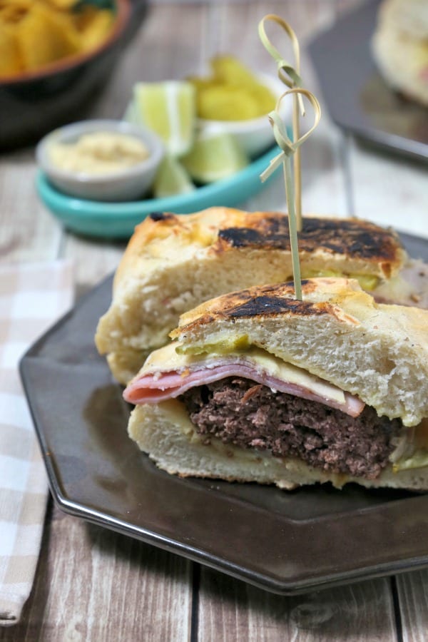 This Cuban Style Burger from CookingInStilettos.com brings all of the familiar flavors of a Cuban sandwich into an epic burger - perfect for your next cookout. Ham, roast pork and swiss are nestled on a pillowy bun with a juicy burger, crisp dill pickles and a mustardy spread | @CookInStilettos