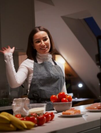 A woman records an online culinary lesson beside fresh food on a kitchen counter