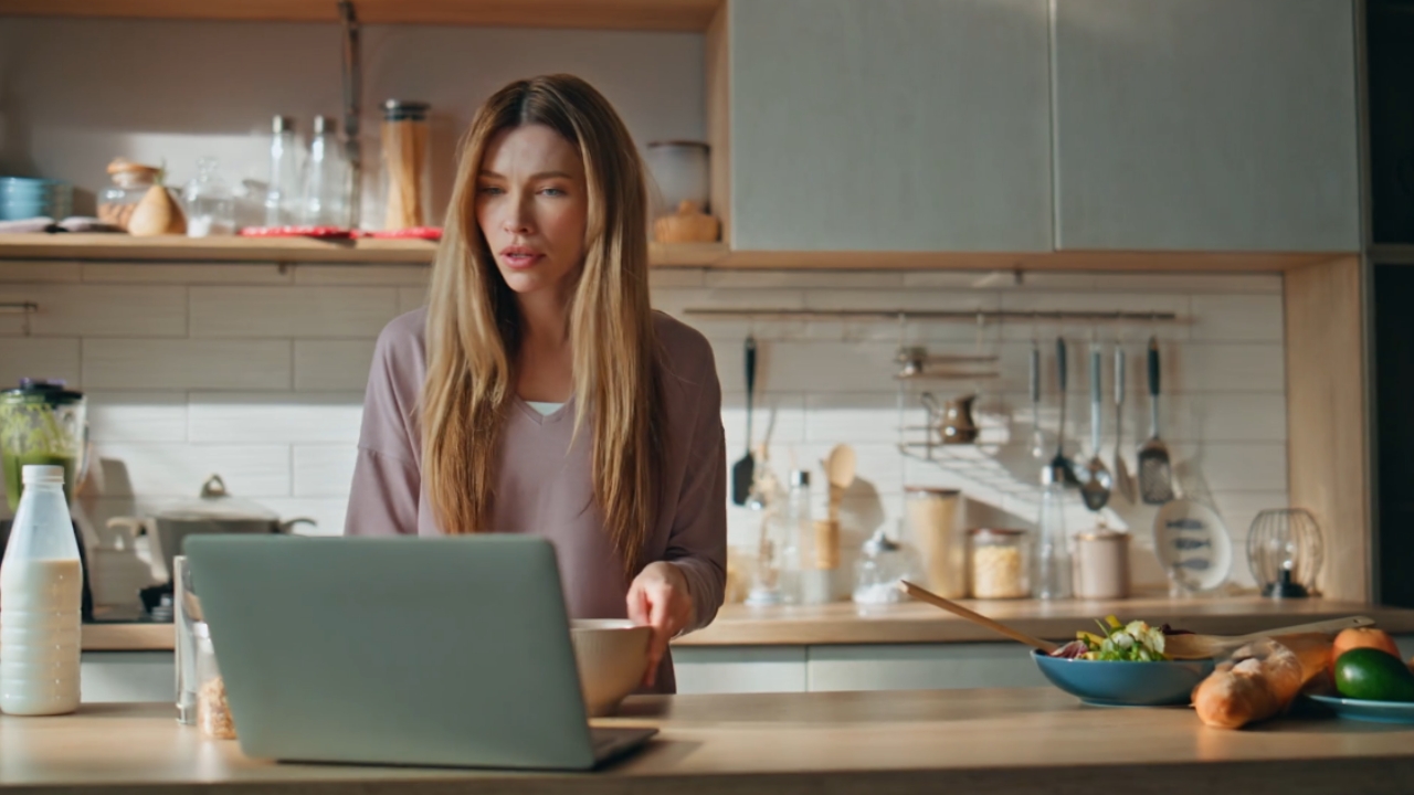 A woman prepares food beside a laptop in a modern kitchen